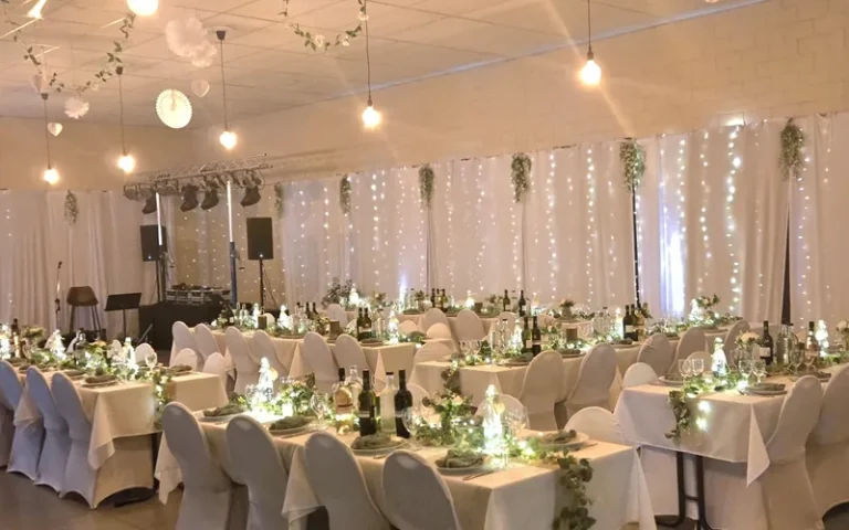 Een trouwfeest in de zaal, met witte stoelhoezen, groendecoratie en lichtjes achter de tafels.