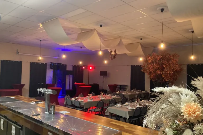 De zaal in de avond, met paarse en blauwe wandverlichting boven de gedekte tafels.