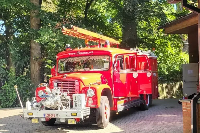 Een oude rode brandweerwagen op de parking voor de zaal.