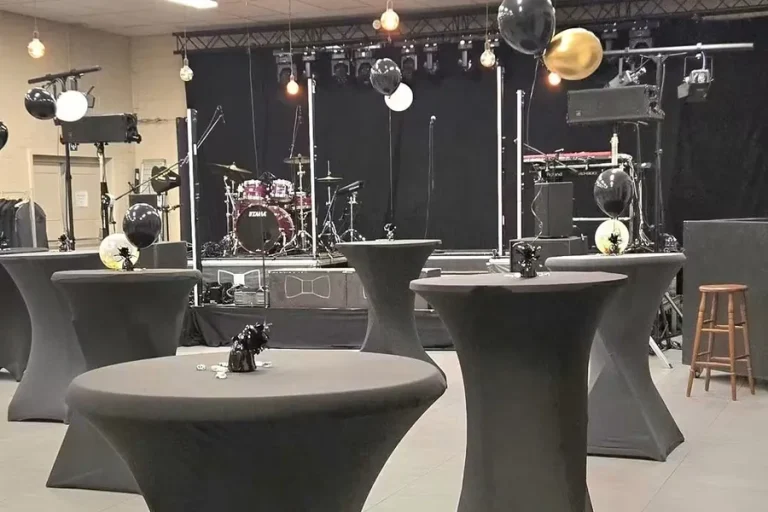 Statafels met zwarte hoezen, ballonnen en een drumstel op het podium.