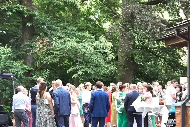 Een receptie op de parking onder de bomen, met gasten in zomerkleding.