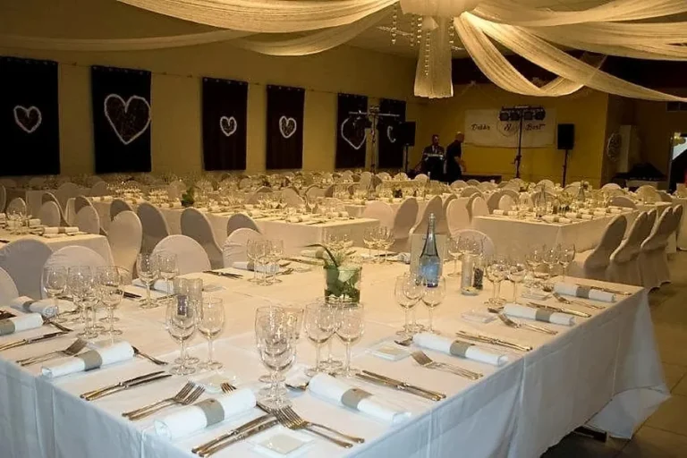 De zaal met gouden doeken, gedekte tafels en gedekte glazen voor een trouwfeest.