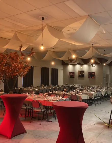 Statafels in de zaal, met warme lampen en witte doeken aan het plafond.