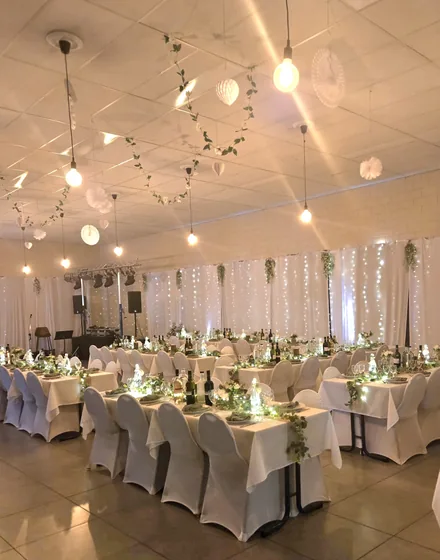 Een trouwfeest met witte stoelhoezen en lichtjes achter de tafels.