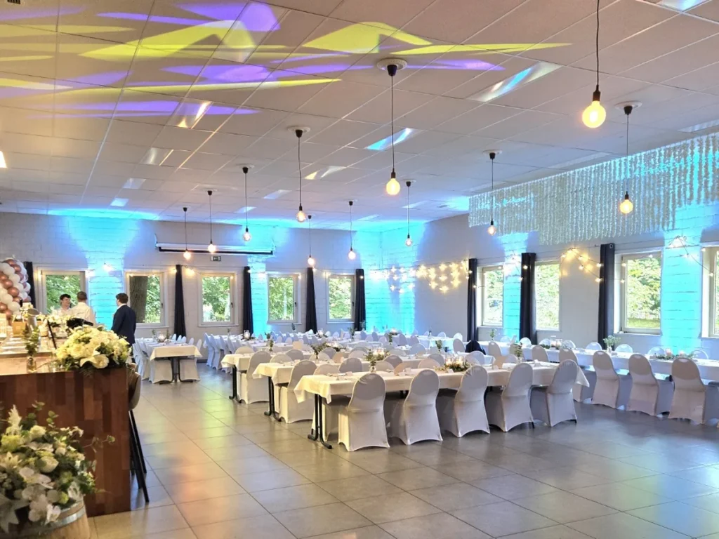 De zaal met lange gedekte tafels, witte stoelhoezen en blauwe wandverlichting tegen de witgeschilderde baksteenmuren.